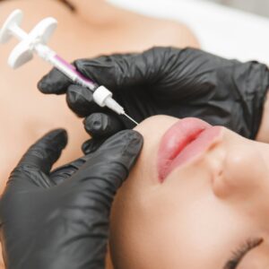A cosmetologist makes lipolytic injections to burn fat on a woman's chin against a double chin.